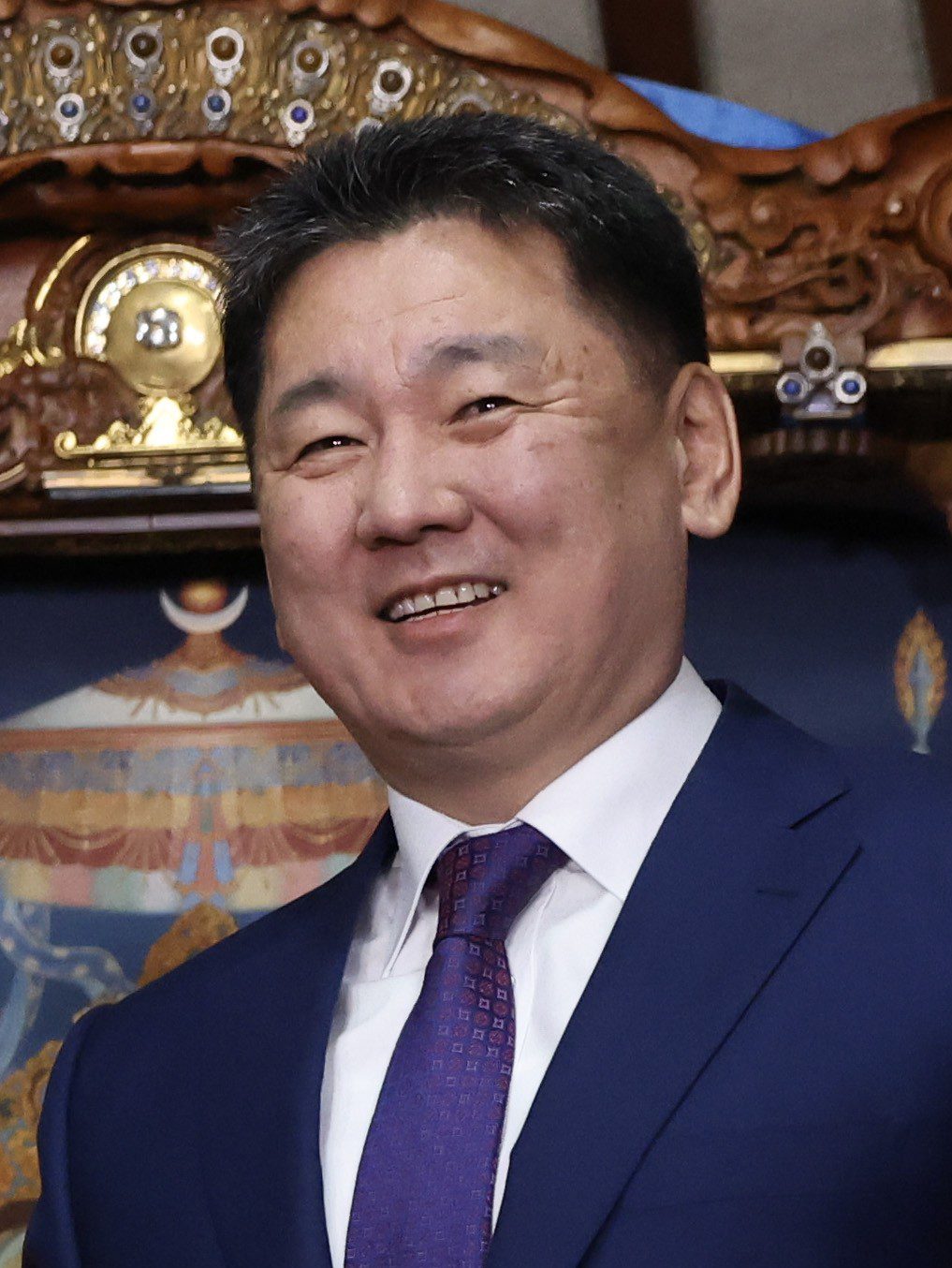 Монгол Улсын Ерөнхийлөгч Ухнаагийн Хүрэлсүх цэнхэр костюм, нил ягаан зангиатай инээмсэглэн зогсож буй нь