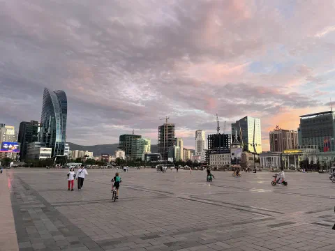 Улаанбаатар хотын төв: Сүхбаатарын талбай, ар талд Blue Sky цамхаг болон өндөр барилгууд, үдшийн ягаавтар тэнгэр